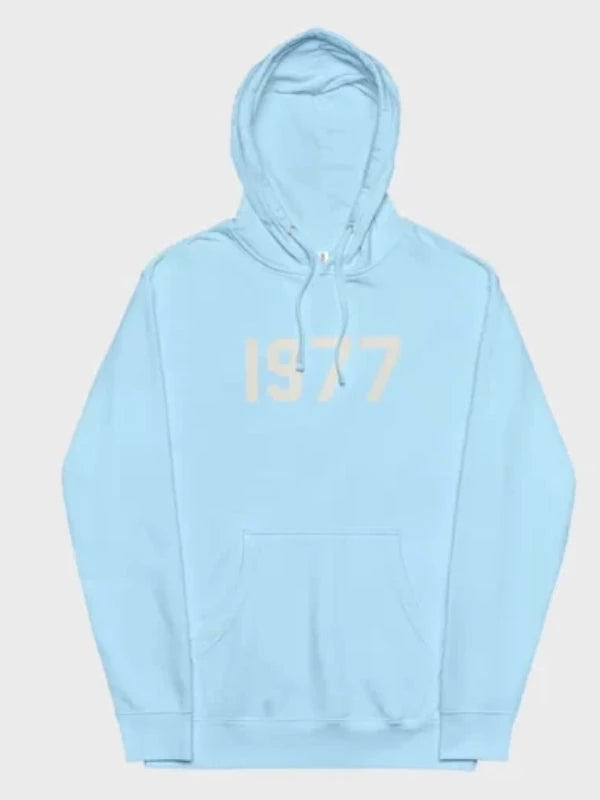 This serene light blue 1977 Essentials Hoodie features the subtle cream-colored numerical design, presenting a fresh and versatile style.