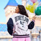 A girl wearing a Disneyland mickey mouse varsity jacket with balloons in the background