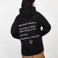 Person wearing a black hoodie with a message on the back, standing against a white background