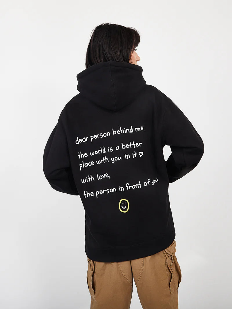 Person wearing a black hoodie with a message on the back, standing against a white background
