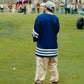 Person in a blue sweater with white stripes on a grassy field, surrounded by spectators.