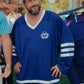 Man wearing a Happy Gilmore 2 Adam Sandler Blue Jersey with a logo, standing outdoors.
