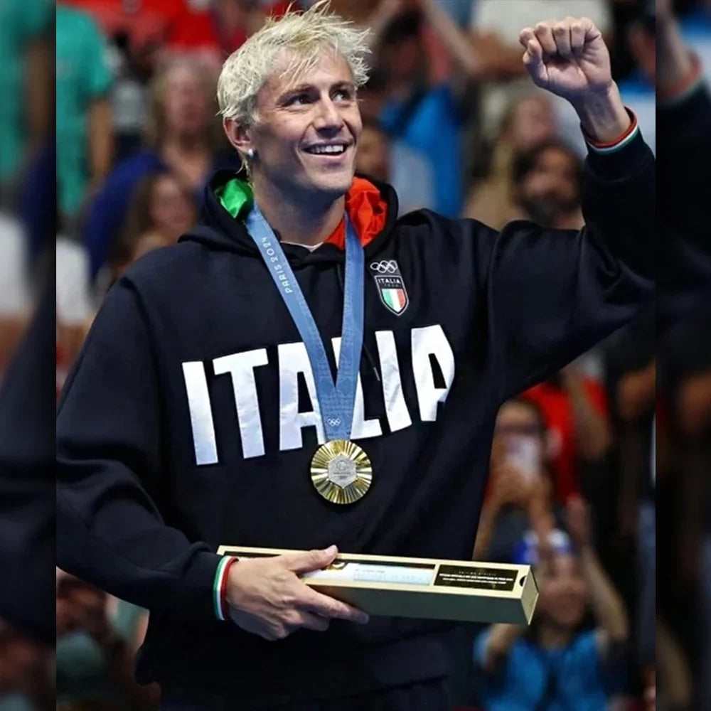 Italian Olympic athlete (male, blonde hair) wearing a black "ITALIA" hoodie with a gold medal.
