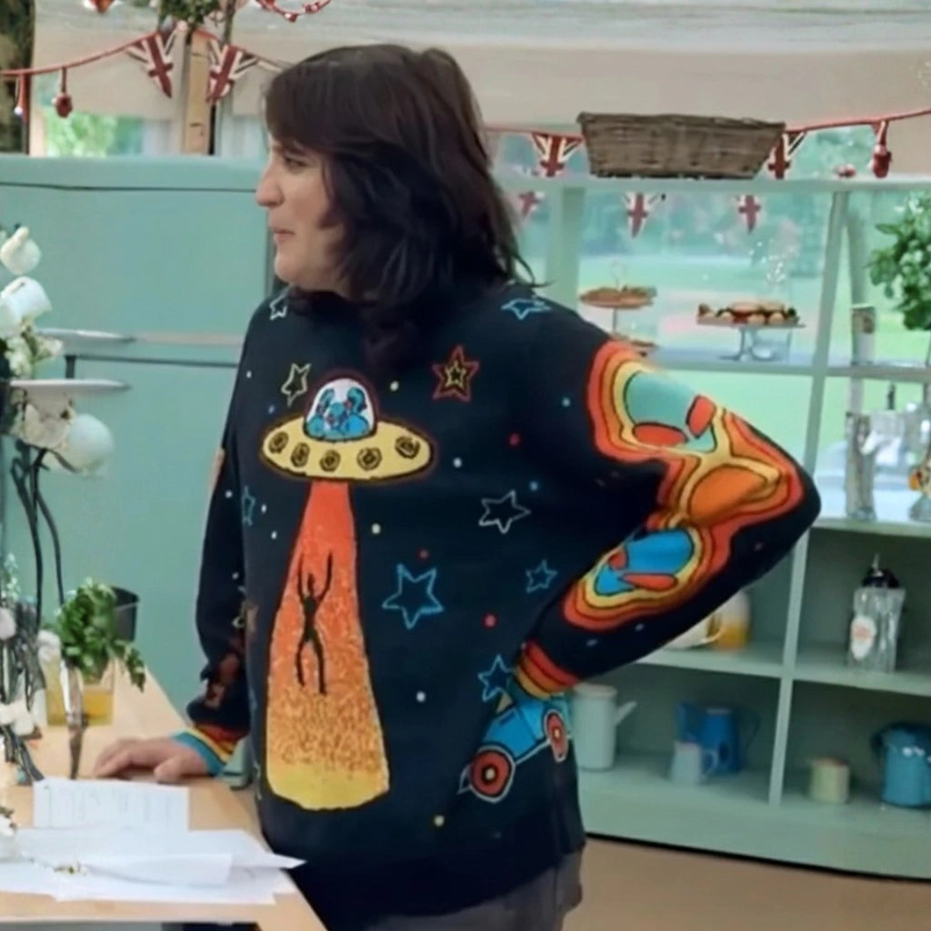 Person wearing a colorful sweater with alien and UFO design in a kitchen setting