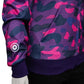 Close-up detail of the ribbed cuff, hem, and front pocket area on a violet, pink, and navy camouflage full-zip hoodie.