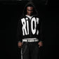 Person wearing a black hoodie with 'RIOT' printed on it against a dark background