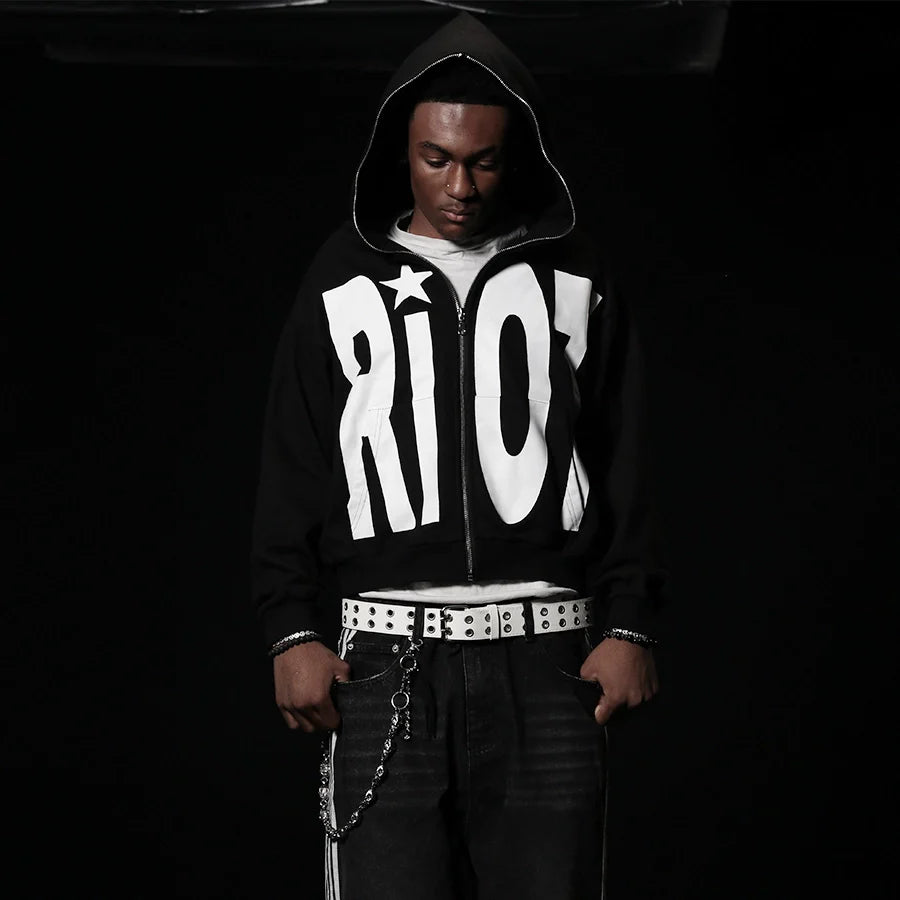 Person wearing a black hoodie with 'RIOT' printed on it against a dark background