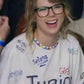 Taylor Swiftwearing a Junior Jewels Shirt with various names printed on it, laughing.