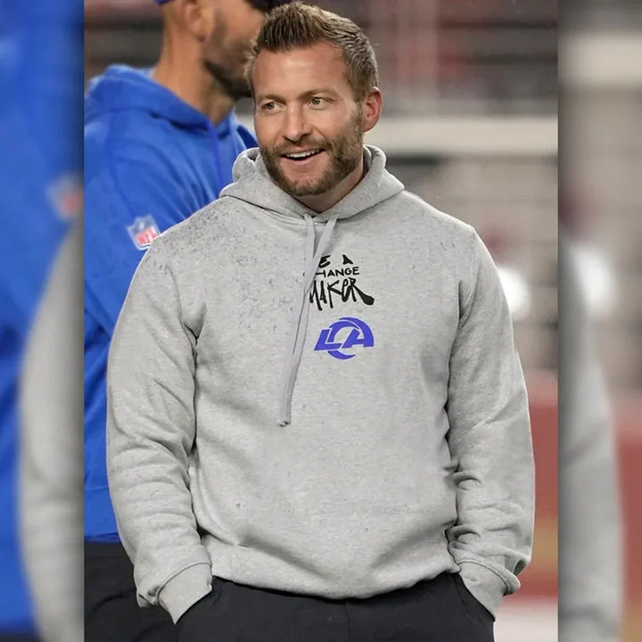 Man wearing a be a change maker nfl hoodie with logos, standing outdoors.