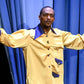 Anthony Mackie wearing a yellow jacket with blue accents in front of blue curtains