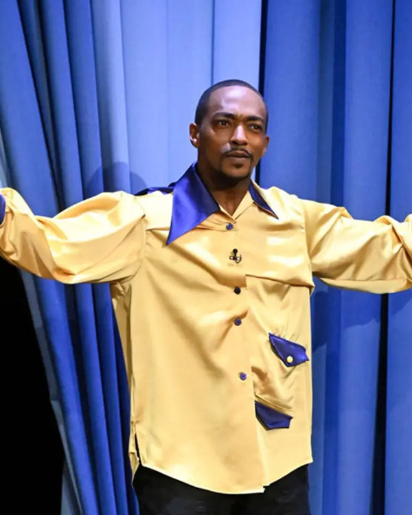 Anthony Mackie wearing a yellow jacket with blue accents in front of blue curtains