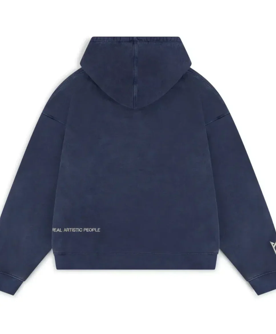 Back view of the oversized navy blue hoodie showing the washed, vintage effect. Small "REAL ARTISTIC PEOPLE" text is visible near the bottom left hem, and a logo detail is on the right wrist.